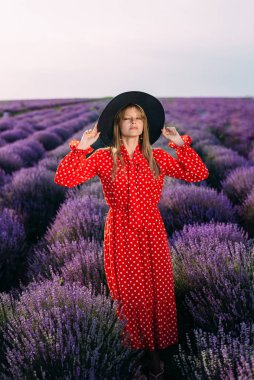 Hasır şapkalı bir kız lavanta tarlasının önünde duruyor.