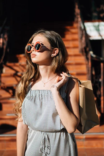 Modell i solglasögon och med en papperspåse bakom ryggen, en flicka med ett köp närbild — Stockfoto