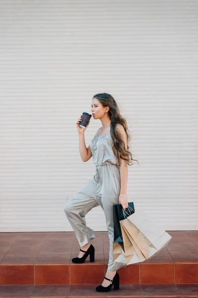 Ung flicka dricker kaffe från en plastmugg efter shopping på trappan — Stockfoto