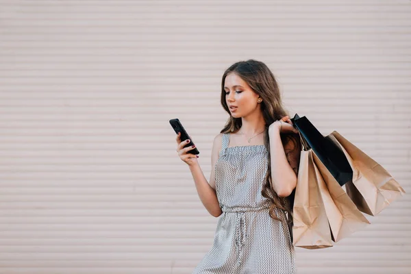 Egy hosszú szőke hajú lány táskákat tart a kezében, és belenéz a telefonba, közelről. — Stock Fotó