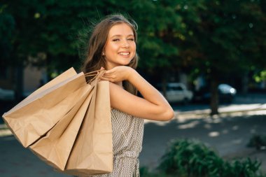 Gülümseyen esmer, butikten aşağı doğru yürür ve alışveriş torbalarını tutar.