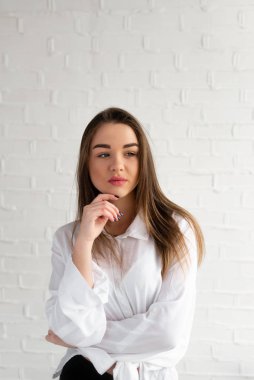 Beyaz arka planda beyaz gömlekli kara kara kara düşünen güzel esmer parmaklarını sakalından tutuyor.