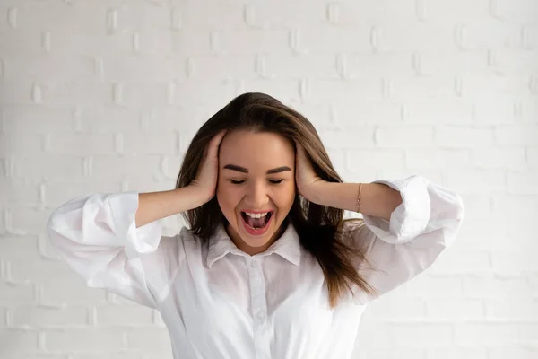 Beautiful brunette in a white shirt holds hands and screams, emotions of anger, white background, — Stock Photo, Image