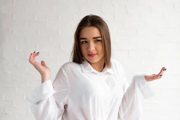 Young beautiful brunette spread her hands and expresses surprise on a white background — Stock Photo, Image