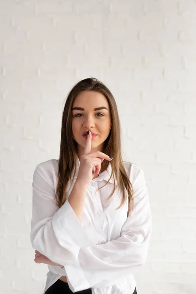 Portrait of a girl offering an index finger to her mouth, showing silence on a white background — Stock Photo, Image