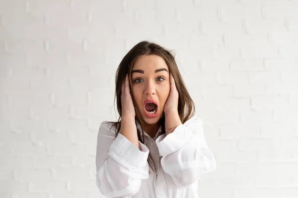 The girl is shocked, holds her hands by her head and the syroko opens her mouth with surprise, white background — Stock Photo, Image