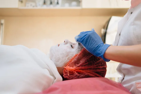 Вид сбоку, врач наносит пациенту косметическую маску для очищения лица, пациент на диване — стоковое фото