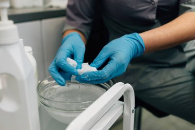 Doktor güzellik uzmanı, hastanın yüzündeki maskeyi çıkarmak için cam pelerinli tamponları sifonu çeker.