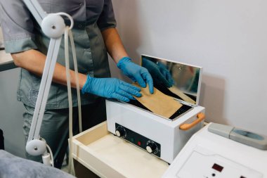 Doktor güzellik uzmanı ofisteki aletten bir balmumu şeridi çıkardı, güzellik prosedürü.