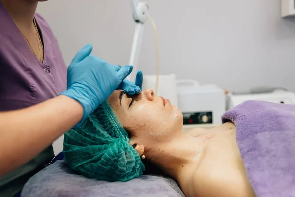 Профиль женщины в синей кепке во время косметической процедуры, доктор гладит ее лицо — стоковое фото