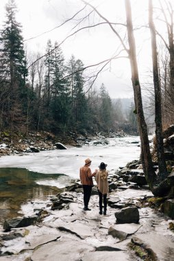 Young stylish couple, guys in love walk in the fresh air. Spring on the street. The river is flowing, the snow is melting and the sun is shining.