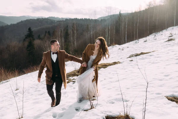 El novio con la novia para dar un paseo por el bosque sobre un fondo de nieve blanca . — Foto de Stock