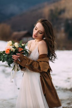 The beautiful bride holds and looks at a wedding bouquet.