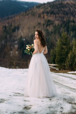 passionate bride in a chic dress looks back holding a bouquet.