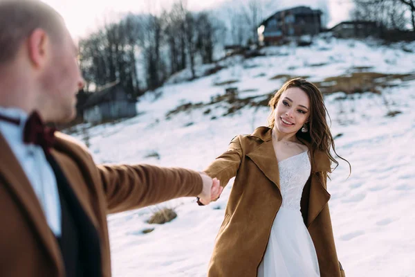 Наречена тримає руку свого нареченого вони обертаються на тлі білого снігу . — стокове фото