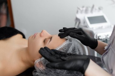 Kadın güzellik uzmanı müşterisiyle spa salonunda çalışıyor. Güzellik uzmanı kızın yüzüne nemlendirici losyon sürüyor. Yüz bakımı. Spa.