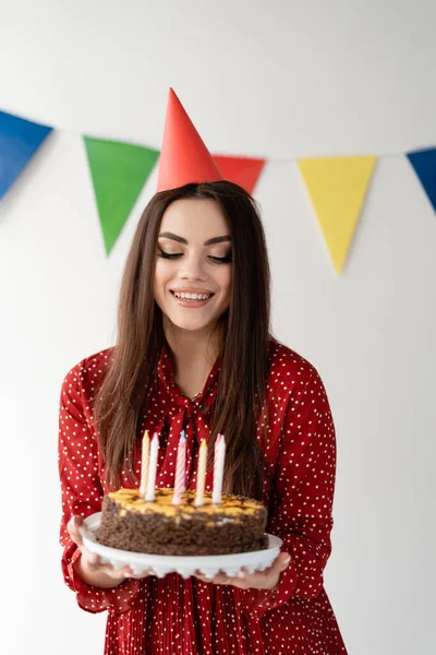 头戴帽子的年轻漂亮的姑娘手里拿着一个漂亮的蛋糕 假日生日 节日期间的蜡烛 幸福在眼睛里 案文的位置 — 图库照片