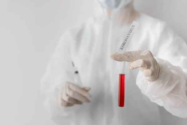 A doctor or laboratory assistant in a protective suit holds a test tube with red liquid. The inscription coronavirus in the laboratory. Caution possible infection. Coronavirus 2019-nCoV vaccine