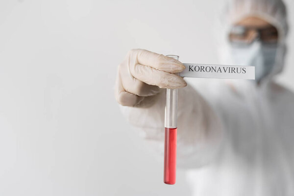 A female doctor in a protective suit, holding a test tube in his hands, the inscription coronavirus. Protection against infection. Test for the presence of a virus in the body. Place for text