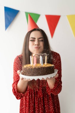 Genç ve güzel bir kız, bir tatil pastasının üzerine mum üflüyor. Evde doğum günü partisi. Metin için yer