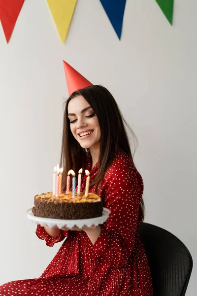 Kadın güzel ve ağız sulandıran bir pasta tutuyor, kafasında kırmızı bir şapka. Tatilin şerefine parti. Tek kişilik doğum günü. Tatil için mumlar.
