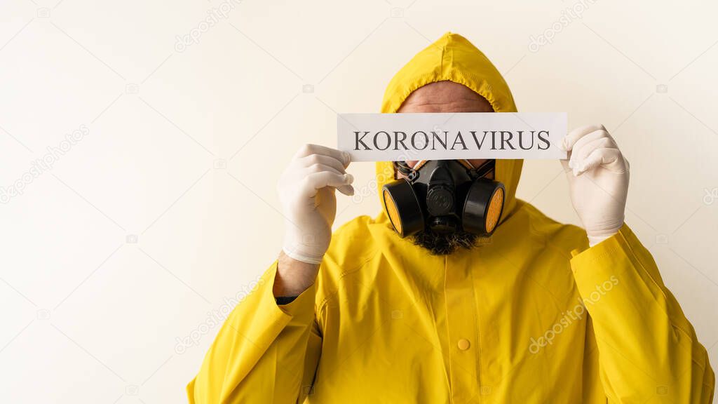 A man wearing a chemical protective suit on a light gray background. Hold in your hands a sheet with the text Coronavirus at the level of your eyes. Hide behind the text. Free place