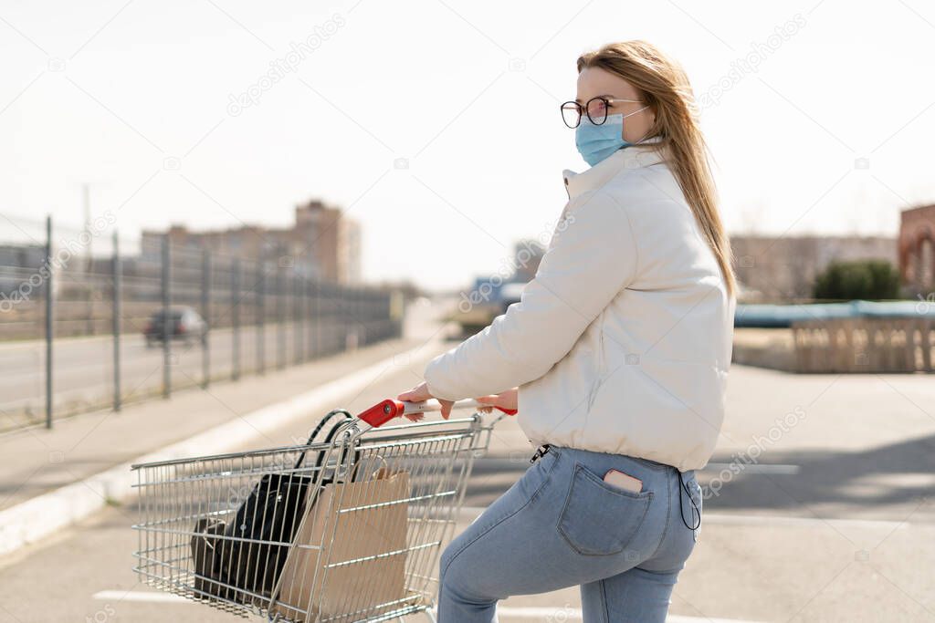 Coronavirus 2019-ncov fight concept, young woman pushing a trolley near supermarket. Purchasing goods during a pandemic. Place for text