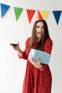 Neşeli doğum günü kadını elinde bir hediye ve yanında şarap bardağı tutuyor. Yüzünde bir gülümseme. Harika bir tatil partisiydi. Metin için yer