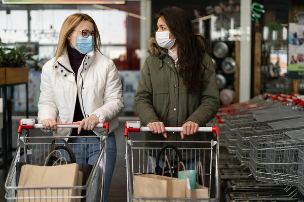 Tıbbi maskeli iki kadın modern bir markete giriyor, bir mağazaya. Coronavirus koruması, karantina, kendini izole etme. Coronavirus Kontrol Konsepti