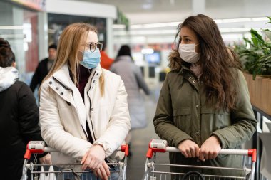 Salgın sırasında iki kadın süpermarketten yiyecek alıyor. Halka açık bir yerde Coronavirus koruma kavramı.