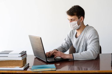 Online eğitim. İnternet üzerinden uzak bir konferansa katılım. Karantinada genç bir adam oturuyor. Koruyucu tıbbi maske takıldı..