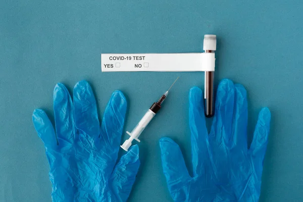 Sur un fond bleu des gants médicaux une seringue avec analyses et une éprouvette avec du sang. Test de dépistage du coronavirus covid-19 — Photo