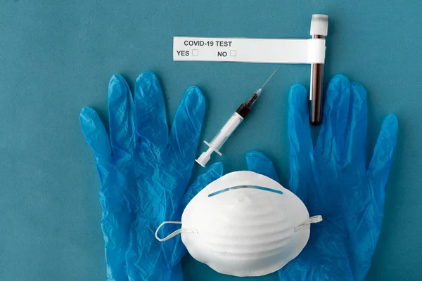 Guanti protettivi medici, un respiratore protettivo, una siringa con test e una provetta con sangue . — Foto Stock