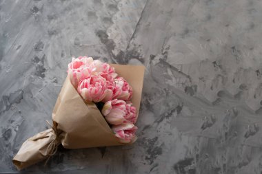 Üst manzara, gri arka planda büyük bir buket pembe lale. Kraft kağıdı sarılı. Metin için yer
