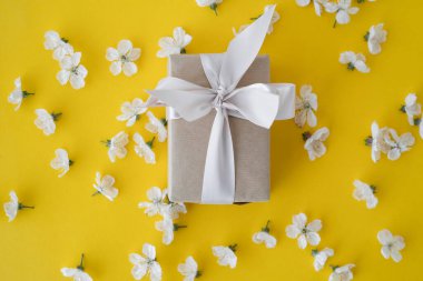 Sarı arka planda çiçekler ve gri bir kutu. Kiraz çiçekleri. Kağıt arka planda kiraz ağacı çiçekleri. Bahar tatili hediye konsepti.