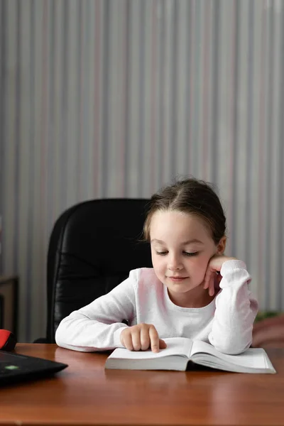 小女孩坐在家里的书桌边看书 手指指示着线条 垂直框架 案文的位置 — 图库照片