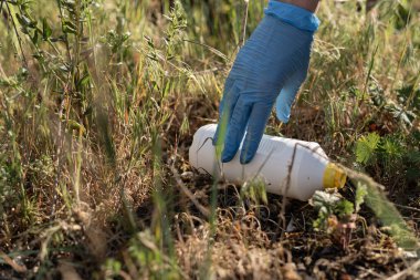 Lastik eldivenli bir kadının elini yakın plan çek. Volontre parkta çöp topluyor. Plastik atık. Çevre kirliliği