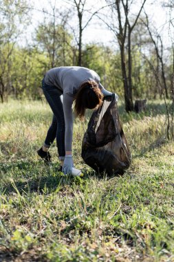 Genç bayan gönüllü olarak parkta çöp topluyor. Çevreyi çöpten koruma kavramı.