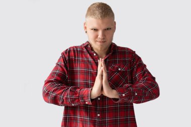 Kafesli, kırmızı tişörtlü genç sarışın adam. Mesaj için beyaz arkaplan yeri. O, ellerini onun önünde bağladı. Kameraya bakıyorum.