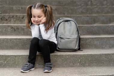Yorgun bir çocuk merdivenlerde oturur. Okuldan sonra dinlenen güzel bir kız öğrenci. Yakınlarda kitaplar ve defterlerle dolu bir sırt çantası var. Çocuklar için boş zaman.