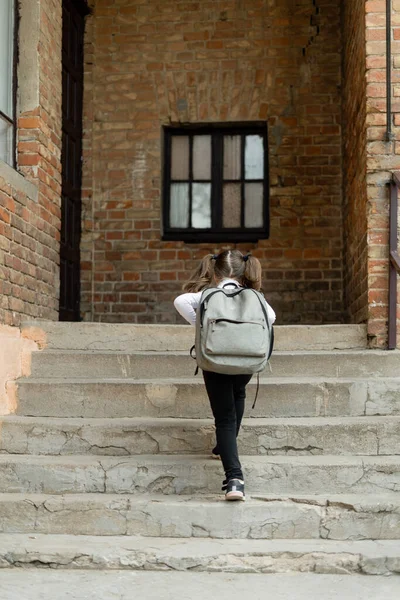 Girl schoolgirl climbs the stairs. She goes to school to get knowledge. On the back of the child is a backpack. Hair is collected in two ponytails. School uniforms and education.