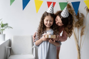 Doğum günü konsepti. Genç anne ve güzel kızı gülüyor, gülüyorlar. Mutlu anne bir hediye verdi ve bebek mutlu. Beyaz arka plan. 7 yıldır. Aile ve eğlence..