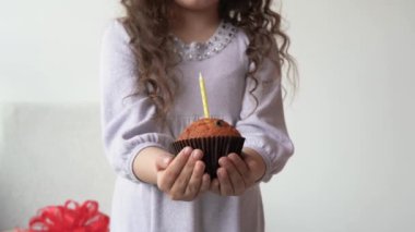 Küçük kız elinde bir kek tutuyor. Annem doğum günü pastasında mum yakıyor. Çocuk tatili konsepti, şekerler.