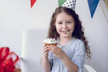 Gülümseyen kız doğum gününde lezzetli bir kek yer. Şenlik şapkası kafaya giydirilmiş. Çocukların doğum günü konsepti