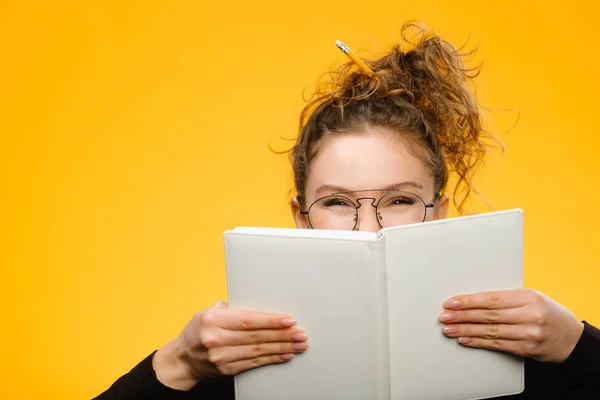 Closeup portrait of teenager hiding behind notebook 스톡 사진