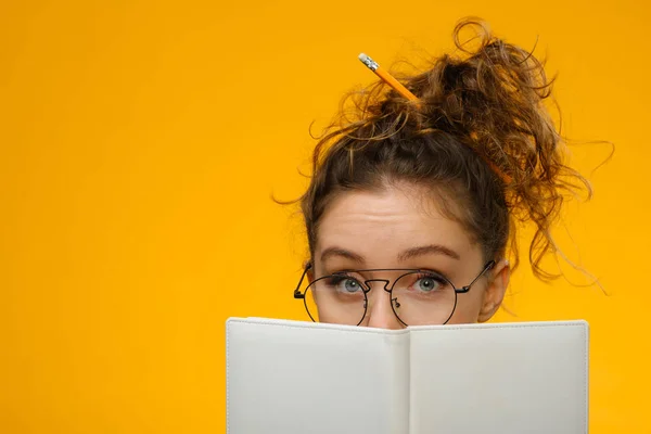 Closeup portrait of teenager hiding behind notebook 스톡 사진