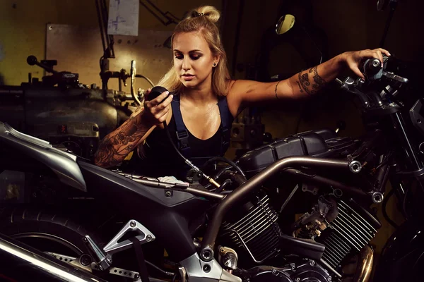 Mujer rubia mecánica reparando una motocicleta en un taller — Foto de Stock