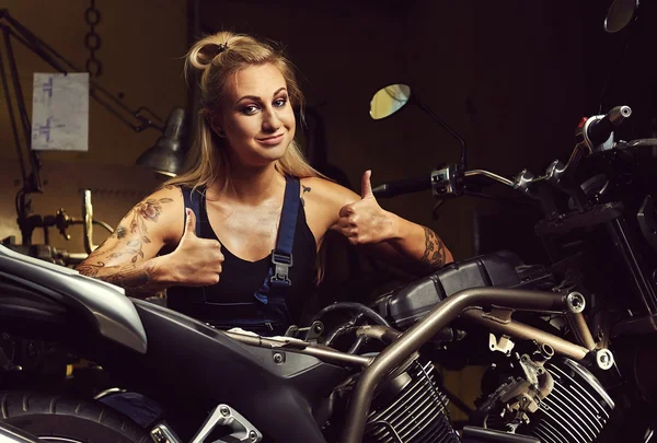 Mujer rubia mecánica mostrando los pulgares hacia arriba en un taller de motocicletas — Foto de Stock