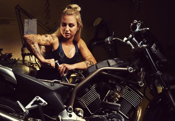 Mujer rubia mecánica reparando una motocicleta en un taller — Foto de Stock