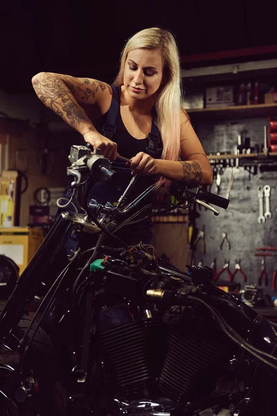 Mujer rubia mecánica reparando una motocicleta en un taller — Foto de Stock